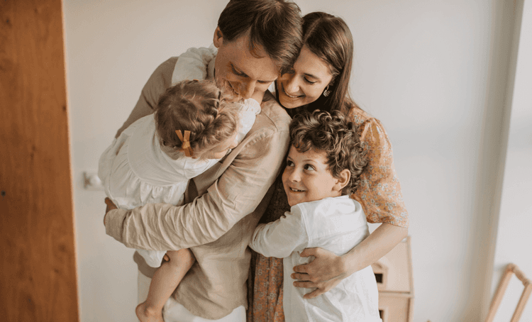 Mum, dad and two kids embracing with smiles on their faces in a home setting